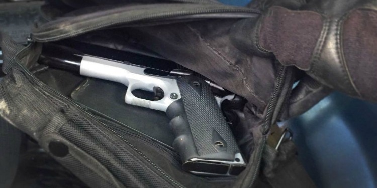 A gloved hand opening a bag with a gun in it.