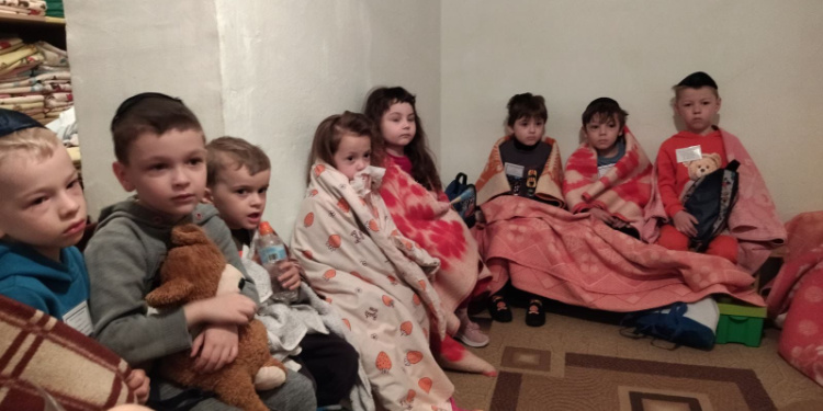 Eight children sitting with blankets while paying attention to someone who's speaking.