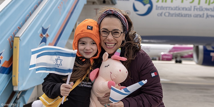 Yael standing with a child in front of a an Aliyah flight holding an Israeli flag