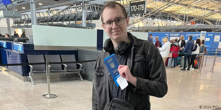 Kostiantyn Kuleshov, oleh from Ukraine, at Vaclav Havel Airport Prague prior to making aliyah. adult man holding passport, black jacket, glasses, black pants, gray luggage bag sitting on ground, smiling, happy