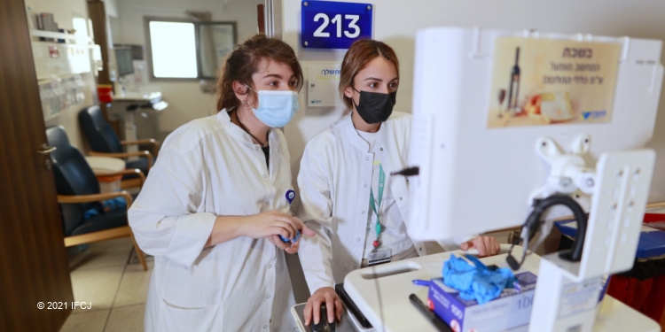 Two girls in masks and lab coats looking at a computer.