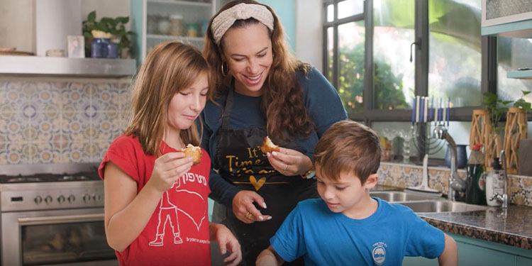 Yael Eckstein and two of her children holding up pieces of latkes.