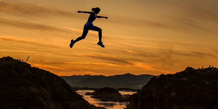 Woman jumping over a river from one side to the other.