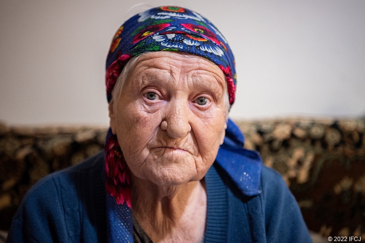 Elderly Jewish woman looking sad and wearing blue and red scarf on her head