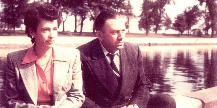 Dated image of a couple sitting alongside a pond.