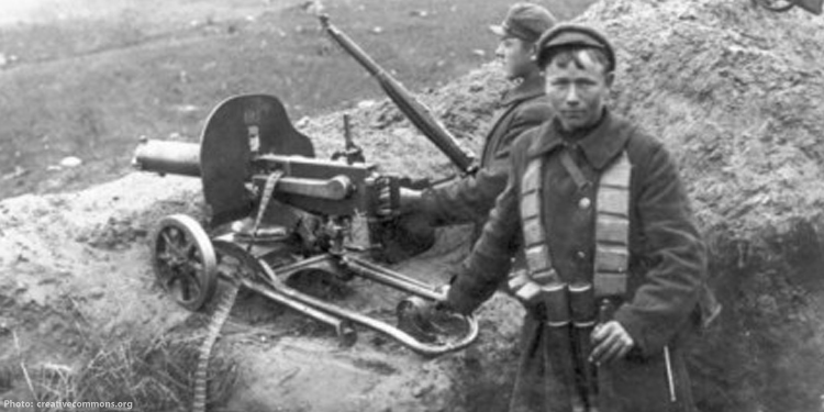 Black and white image of Lithuanian soldier standing next to a machine gun.