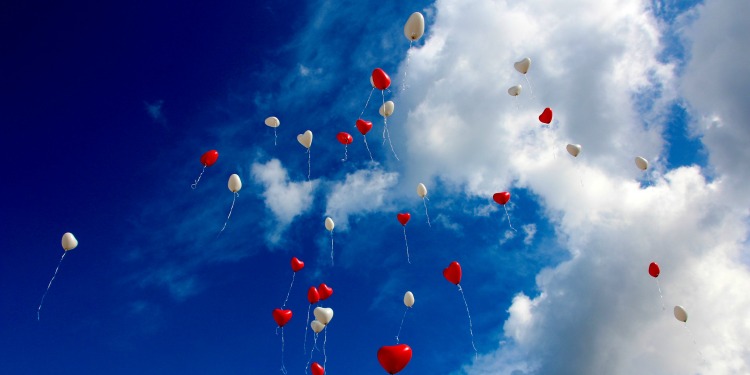 Red and white heart shaped balloons flying up in the sky.