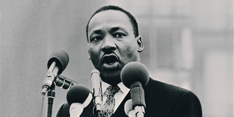 Photo of Martin Luther King speaking into multiple microphones in front of podium