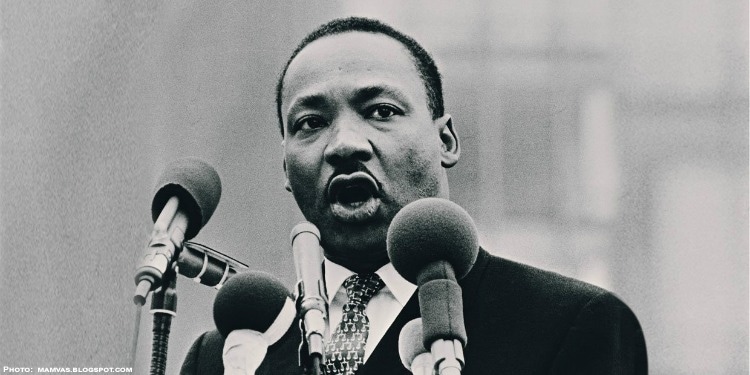 Black and white image with four microphones in front of him speaking.