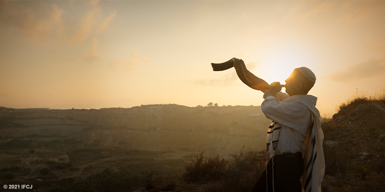 Man blowing a shofar at the top of a hill during dawn.