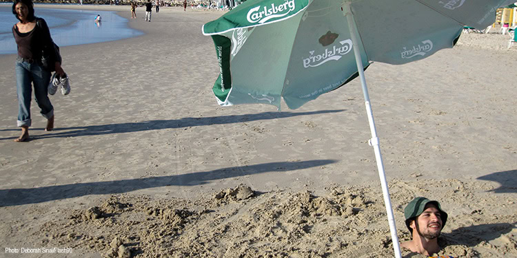 Man buried in the sand up to his neck at the beach.