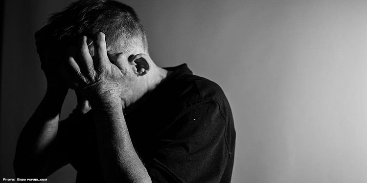 Black and white image of a man holding his head in his hands.