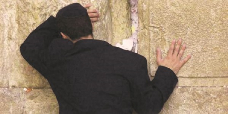Jewish man praying at the Western Wall with his hands touching the wall.