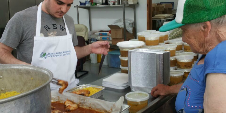 IFCJ volunteer serving a hot meal to an elderly woman.