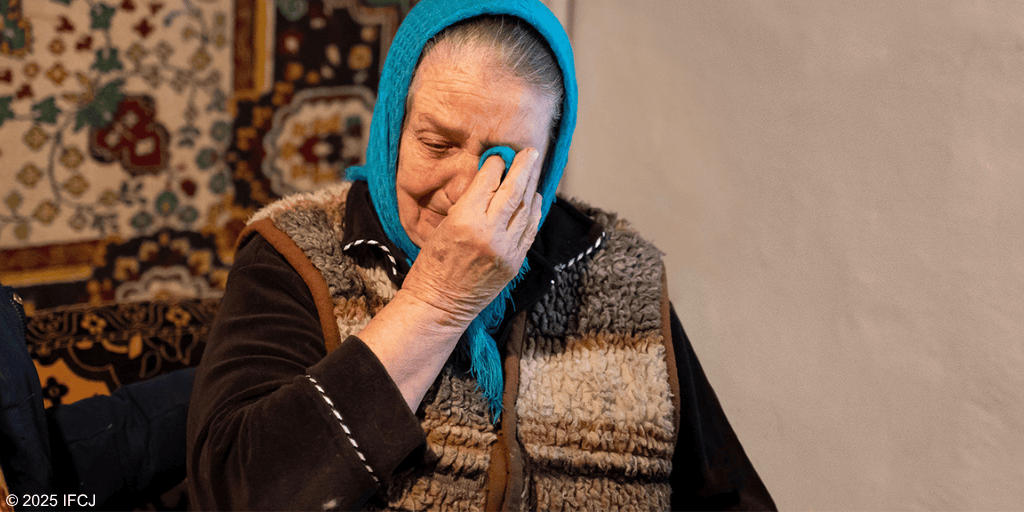 An elderly woman with a blue headscarf and warm clothing expresses emotion, symbolizing compassion and kindness in a heartfelt moment.