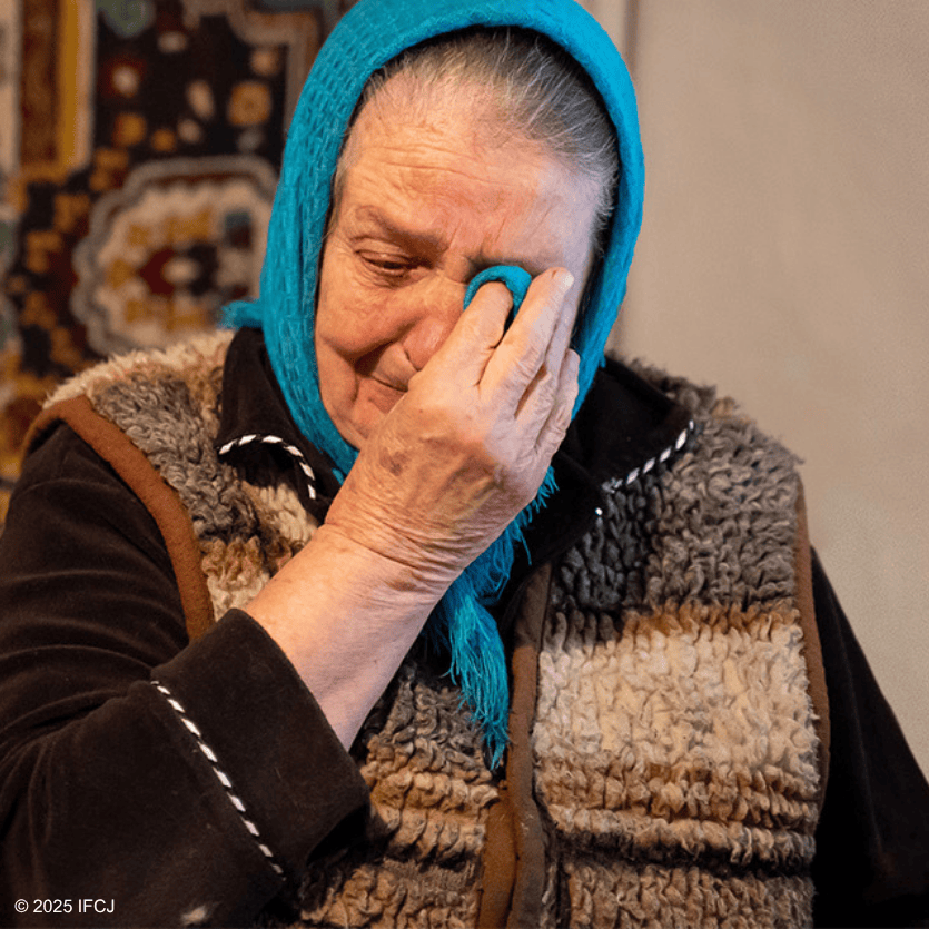 An elderly woman with a blue headscarf and warm clothing expresses emotion, symbolizing compassion and kindness in a heartfelt moment.