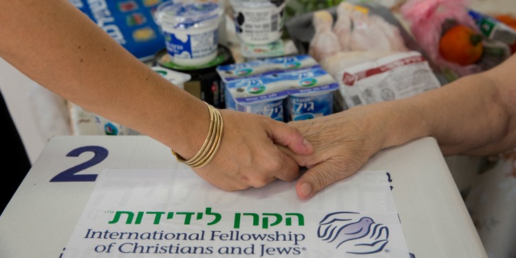Yael Eckstein holding elderly woman's hand on Rosh Hashanah food box