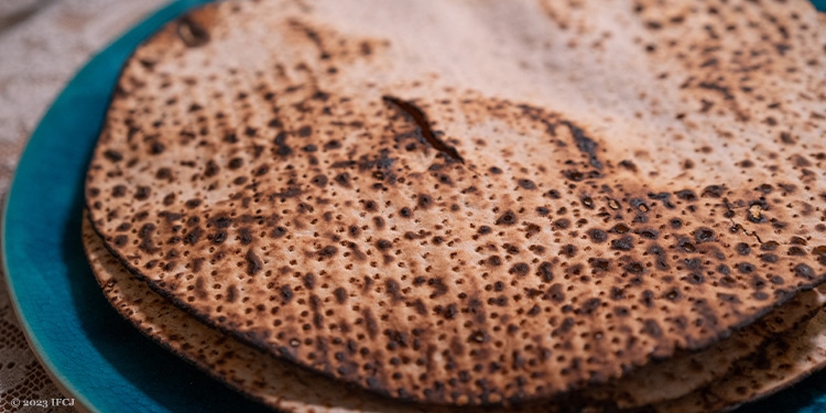 Close up image of several pieces of matzah laid on top of each other on a blue plate.