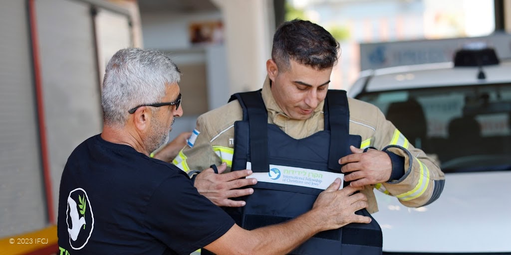 IFCJ volunteer helping a firefighter put on an IFCJ branded flak jacket