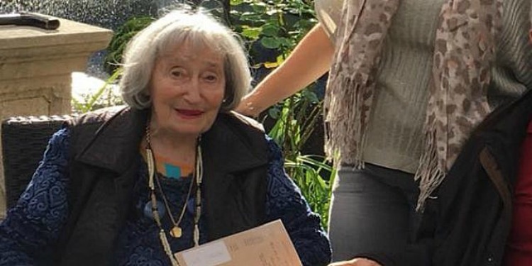 Elderly woman sitting in a chair, while soft smiling.