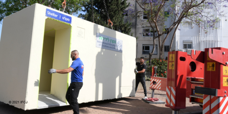 Two men moving an IFCJ mobile bomb shelter in Ashkelon.