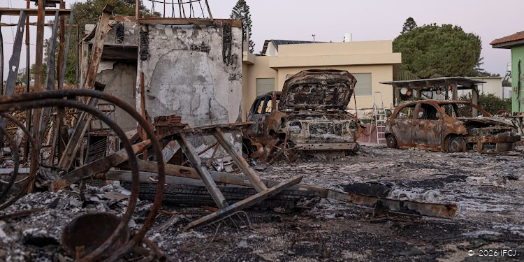 Burned and charred vehicles in a scene of destruction, with damaged structures and debris scattered around, indicating recent fire damage.