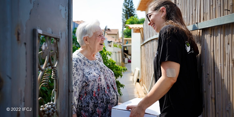 IFCJ staff member greeting Ukrainian refugee Nataliia Berkhstein with an IFCJ food box in hand.