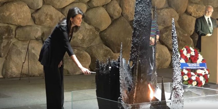 Woman helping to light a sculpture as a man at a podium watches her.