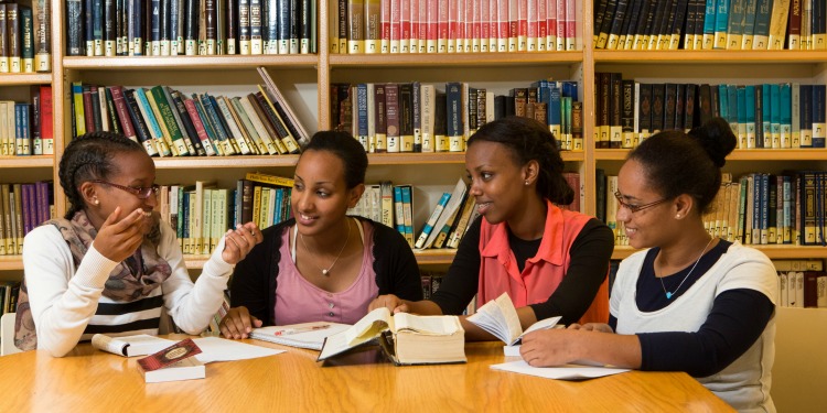 Four young Ethiopian girls a part of the Nishmat Maayan Program reading books together in a library.