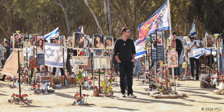 People gather at a memorial site with photographs, flags, and flowers to commemorate Tisha B’Av, a day of mourning in Jewish tradition.