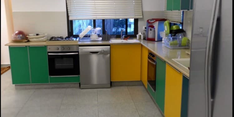 A kitchen with green and yellow cabinets, along with updated appliances.