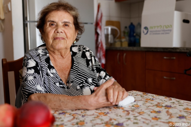 Elderly Jewish woman sitting at table with fruit.