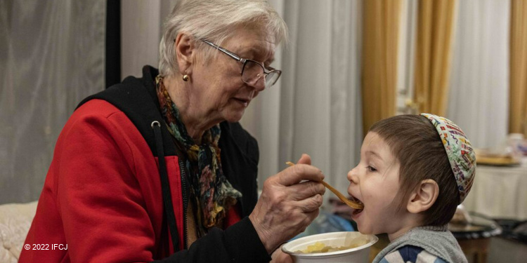 Elderly Jewish woman feeding a young boy with a kippah on.