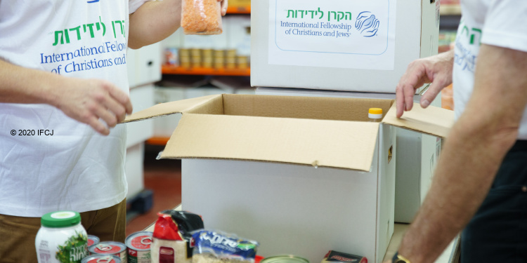 Close up image of two IFCJ staff members packing food boxes.