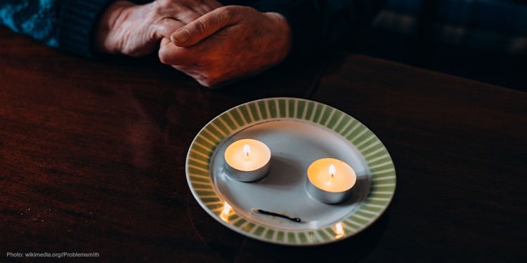 Pair of hands in front of two candles on a plate