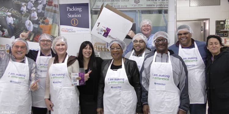 Nine IFCJ staff members and Yael Eckstein packing food for IFCJ food boxes together.