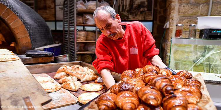 An elderly man adjusting a pan full of bread.