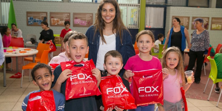 Young woman standing with a group of kids holding red bags that read FOX: Basic is Beautiful.