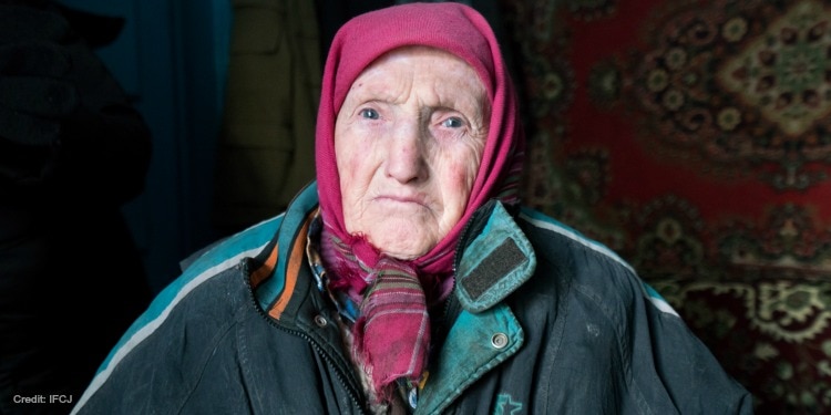 Elderly Jewish woman in a pink head scarf and blue jacket looking straight ahead.