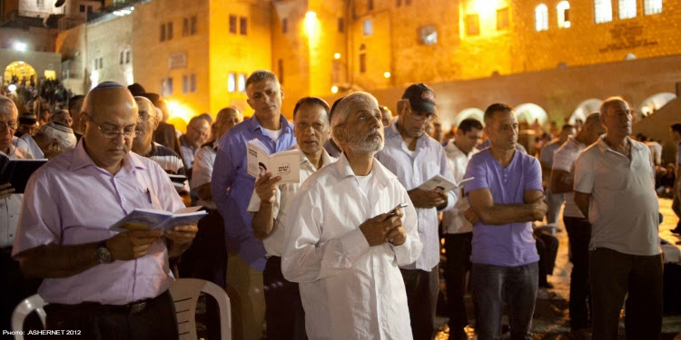 Several men looking up into the sky while praying at the Western Wall.