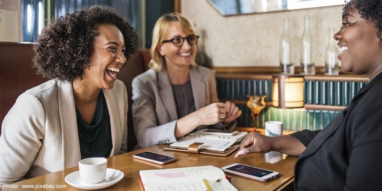 Three women laughing and talking over coffee.