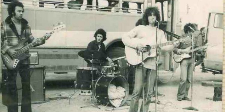 A rock band performing beside a bus.