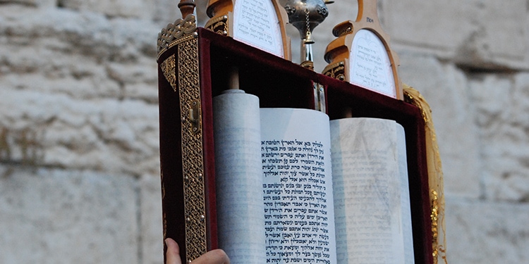 A scroll with Jewish writing on it held up in front of the Western Wall.