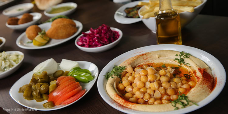 A diverse Middle Eastern food platter featuring chickpeas, pickles, salads, and condiments, served on a dark table.