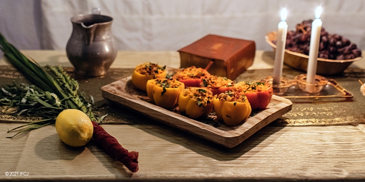 A wooden table with candles, a pitcher, stuffed peppers, and more.