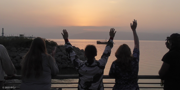 Five individuals raising their hands while looking over the sunset.