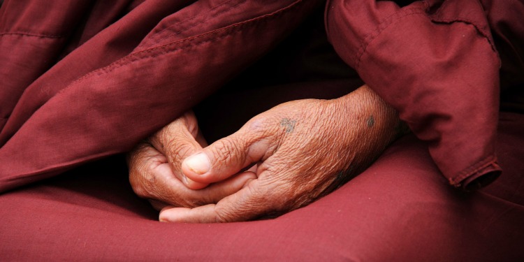 Two older hands folded together in prayer against a red background.
