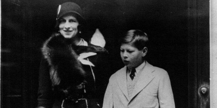 Black and white image of a woman dressed in fur walking alongside a young boy in a suit.