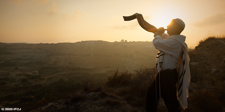 Jewish man blowing the shofar on a hilltop.