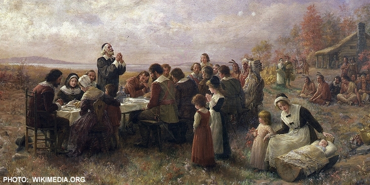 Painting of people having a meal together in a field.